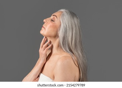 Feminine Senior Lady With Silky Skin Wearing Towel, Touching Her Neck On Grey Studio Background, Side View Portrait. Sensual Mature Woman With Natural Beauty Taking Care Of Her Face And Body