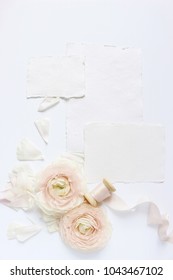 Feminine wedding, birthday desktop mock-up scene. Blank craft paper greeting cards, silk ribbon and blush pink Persian buttercup flowers. White table background. Flat lay, top view.