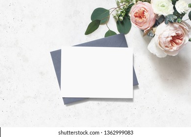 Feminine wedding, birthday mock-up scene. Blank paper greeting card, envelope. Bouquet of eucalyptus leaves, blush pink English roses and ranunculus flowers. Concrete table background. Flat lay, top 