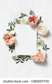 Feminine Wedding, Birthday Mock-up Scene. Blank Paper Greeting Card. Floral Frame Of Blush Pink English Roses, Ranunculus Flowers And Lentisk Leaves. Concrete Table Background. Flat Lay, Top View.