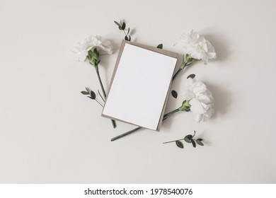 Feminine  Wedding, Birthday Stationery Composition. Blank Greeting Card, Invitation Mockup With Craft Envelope. White Carnation Flowers And Eucalyptus Branches Isolated On Table Background. Flat Lay, 