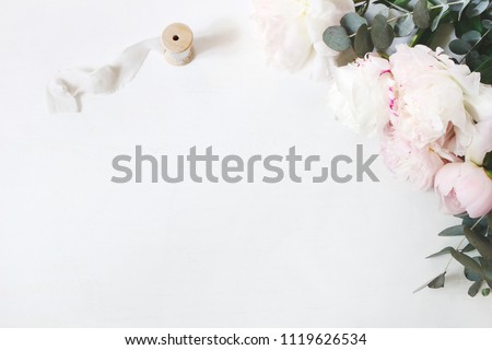 Feminine wedding or birthday table composition with floral bouquet. White and pink peonies flowers, eucalyptus and silk ribbon. Festive greeting card, invitation. Empty space. Flat lay, top view.