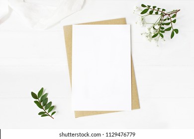 Feminine wedding stationery, desktop mock-up scene. Blank greeting card, craft envelope, baby's breath flowers, silk ribbon and lentisk branches. Old white wooden table background. Flat lay, top view. - Shutterstock ID 1129476779
