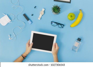 Feminine Workspace Concept. Female Hand Holding White Tablet On Blue Background. Flat Lay, Top View