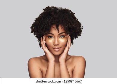 Femininity. Attractive Young African Woman Applying Medical Eye Patch And Smiling While Standing Against Grey Background