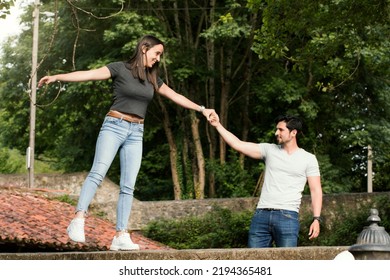 Feminism And Equality. Social Balance Between Women And Men. Woman Balanced On A Wall Helped By A Man. Woman In Balance With Her Partner. Concept Of Equality Between Men And Women Working Together