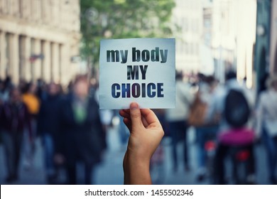 Feminist hands holding a protest banner with the message my body my choice over a crowded street. Human rights concept against fetus law and reproductive justice. Stop discrimination and injustice.
