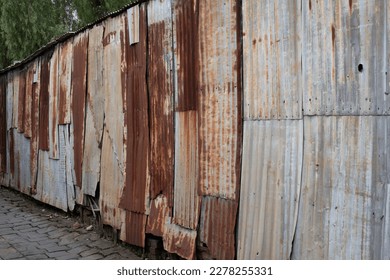 Fence in an alley made of rusted iron sheet metal and corrugated iron that are fastened together - Shutterstock ID 2278255331