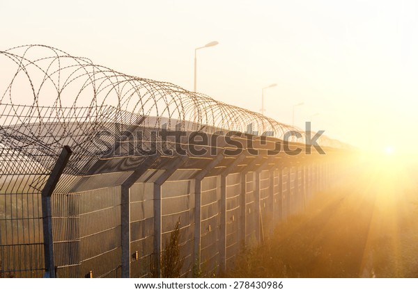 fence with barbed wire on the border\
of the object at dawn with fog in the summer,\
russia