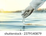 Fence, check the water sample for infections. Gloved hand with flask and a test tube on a background of lake, river, sea. Pollution of ecology, environment