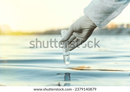 Fence, check the water sample for infections. Gloved hand with flask and a test tube on a background of lake, river, sea. Pollution of ecology, environment