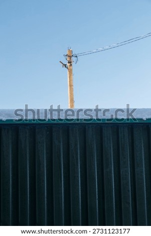 
The fence in the foreground frames a view of a metal power line pole with high-voltage wires strung up, covered in snow and frost. The winter landscape highlights the blend of nature and human infrastructure on the cottage property. Ideal for energy, utilities, and winter details.
utility pole fence