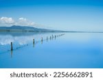Fence leading into calm blue water of Lake Wairarapa with distant hills across other side in New Zealand North Island.