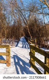 A fence lined entry way to a wooden walkway covered with snow in Frick Park located in Pittsburgh, Pennsylvania, USA on a sunny winter day