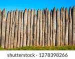 Fence made of sharp wooden stakes against the blue sky. Wooden fence vertical logs pointed against the sky protection against invaders and wild animals. Ancient stockade