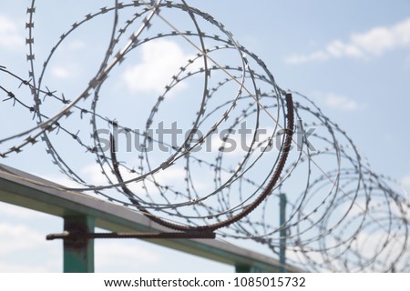 Fence with razor barbed wire protection against blue sky background. Dictatorship and tyranny concept