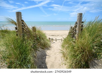 Fenced path through sand dunes leading down to a sandy beach on a sunny summer day. Gouville sur Mer, France.