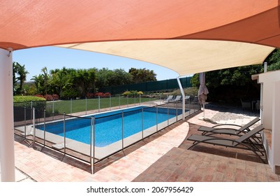 Fenced swimming pool in garden with sunbeds under a shade sail