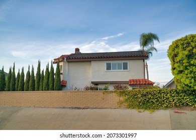 Fenced Two-storey House With Tall Narrow Trees And Crawling Plants Outdoors At Southern California