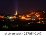 Fench village at night, all illuminated, church tower with a light beam to the dark sky