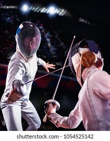 Fencing sport for women fencer. Fia female athlete in fight epee competition. Large group fans on tribunes with lens flare illumination.