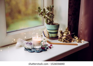 Feng Shui altar at home in living room or bed room. Attracting wealth and prosperity concept. Crystal clusters, wire tree with gemstones, golden smiling Buddha figure on table window sill. 