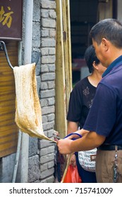 Fenghuang, China - September 12, 2007: A Local Chinese Man Pulling Taffy Candy Attached To A Hook On An Outdoor Wall On The Street