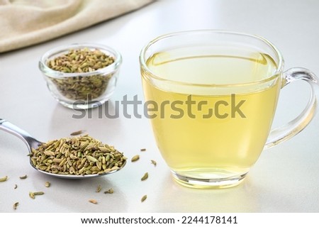 Fennel seed water in a glass cup with fennel seeds in the background.