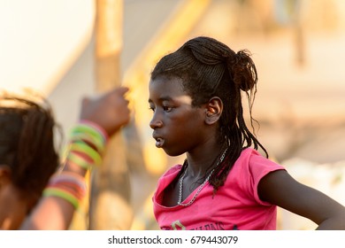 FERLO DESERT, SENEGAL - APR 25, 2017: Unidentified Fulani Little Girl With Braids In Pink Shirt Stands On The Street. Fulanis (Peul) Are The Largest Tribe In West African Savannahs