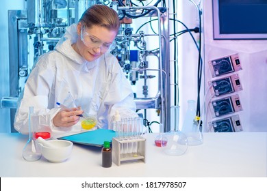 Fermentation Reactions In Pharmacology. The Girl Is Sitting At A Table With Chemical Dishes. Girl On The Background Of A Laboratory Bioreactor. Microbiological Examination.