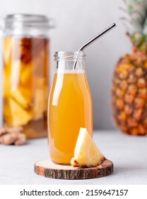 Fermented pineapple beverage tepache in reusable glass bottles with metal drinking straws and glass pitcher on light gray background