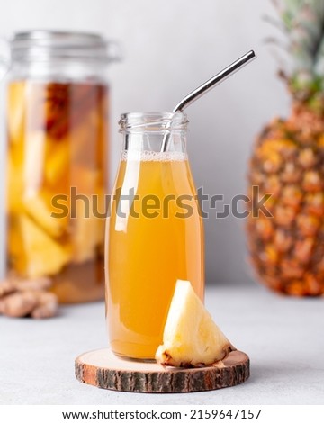 Fermented pineapple beverage tepache in reusable glass bottles with metal drinking straws and glass pitcher on light gray background