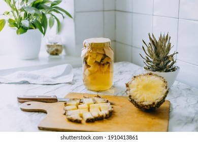 Fermented pineapple kombucha drink tepache. Cooking process of homemade probiotic superfood pineapple beverage. Drink jar and sliced pineapple on home kitchen.
