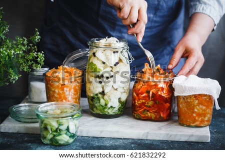 Fermented preserved vegetarian food concept. Cabbage kimchi, broccoli marinated, sauerkraut sour glass jars over rustic kitchen table. Canned food concept.