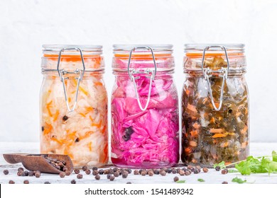 Fermented preserved vegetarian food. Homemade marinated cabbage kimchi, sea kale with carrot, sauerkraut sour in glass jars on rustic wooden kitchen table. Canned vegetables food concept