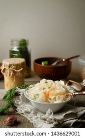 Fermented shredded cabbage in a bowl and in a glass jar, pickled cucumbers on a wooden rustic background. Vertical image.