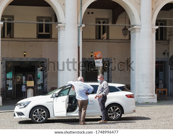 Ferrara, Italy - June 2, 2020. Taxi driver and\
customer next to a taxi. Both people with protective mask on face\
against Coronavirus,\
Covid-19.