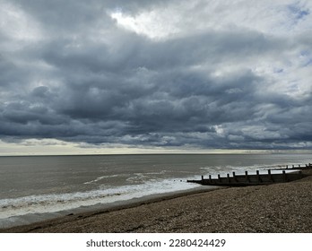 Ferring pebble beach with stormy clouds before the rain. The tide is coming in at about 2pm. The dark clouds contrast with the band of blue sky with the murky sea and break water. 26th March 2023 