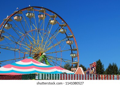 Ferris Wheel At A County Fair With Blue Sky In The Background And A Colorful Striped Tent In The Foreground