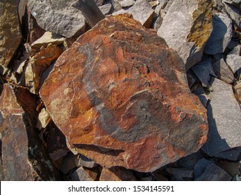 Ferrous quartzite stone lying on other quartzites on forest floor, a look from above. The rock is of red color, with rusty appearance. Shot in Brdy hills, Czech republic.