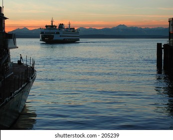 A ferry arriving at the Seattle waterfront during sunset with the Olympic Mountains as a backdrop.
