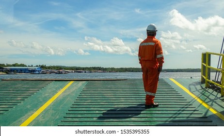 Ferry Ship Crew Worker In Coveralls Standing On Edge Of Deck While The Ferry Moving Toward Of Shore.