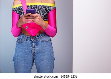 Festival Look Disco Girl, Outfit Details. Female Model 80s Jeans, Colorful Top And Neon Pink Fanny Pack. Smart Phone Self Check In