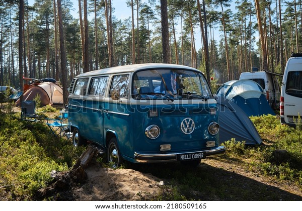 Festival mobile homes in coniferous forest. Camping\
for tents and cars. Mobile home based on retro Volkswagen\
Transporter minivan blue chrome wheels and mirrors. Leningrad\
Region, Russia - June\
2022.
