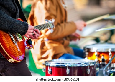 Festival music band. Hands playing on percussion instruments in city park . Drums with sticks closeup. Body part of male musicians. Sharpen is guitar and man hand. - Shutterstock ID 583766131