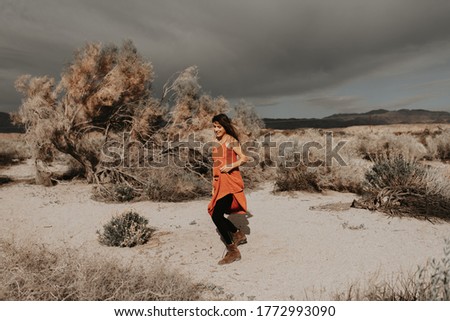 Festival vibes. Happy hipster girl jumping and dancing with windy hair in desert nature holding a backpack. Young hipster traveler girl in gypsy look, in Coachella Valley in Southern California
