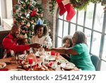 Festive African American family dinner, celebrating Christmas. Smiling adults and children enjoy holiday meal by tree. Joyful holiday gathering. African American family celebrating, Christmas dinner.