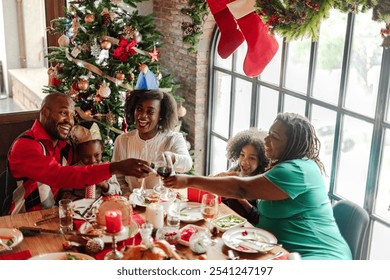 Festive African American family dinner, celebrating Christmas. Smiling adults and children enjoy holiday meal by tree. Joyful holiday gathering. African American family celebrating, Christmas dinner. - Powered by Shutterstock