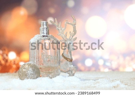 festive background of blurred lights in shades of gold with Christmas toys, deer, ball and perfume bottle on the snow. Greeting Christmas card. Presentation of perfumes.
