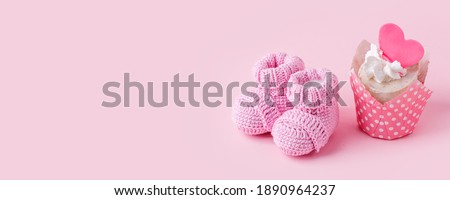 Festive background decoration for birthday celebration with delicious сupcakes and knitwear booties for a baby shower on pink background, first birthday concept, party, monochrome, banner